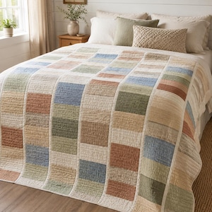 Può includere: Un copriletto trapuntato caratterizzato da un motivo a righe verticali composto da blocchi alternati in tonalità tenui di blu, verde salvia, terracotta e crema. Il tessuto presenta una texture cucita visibile su tutta la superficie.