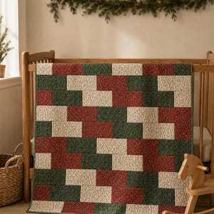 May include: A rectangular quilt featuring a repeating geometric pattern of interlocking blocks in dark green, deep red, and cream. Each block is composed of a small-scale floral print fabric, finished with a dark green border trim along the edges.