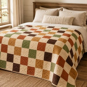 May include: A quilt featuring a repeating checkerboard pattern in alternating squares of cream, sage green, burnt orange, and dark brown. The fabric has a visible quilted texture throughout, covering the top of a bed with matching pillows.