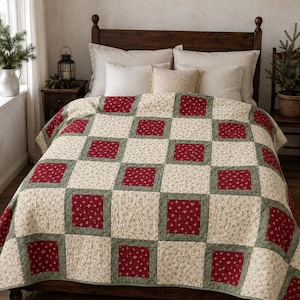Puede incluir: Una colcha de patchwork con un patrón de cuadrícula repetitivo de cuadrados florales de color rojo intenso, cuadrados sólidos de color verde salvia y cuadrados florales de color crema. La colcha cubre una cama y muestra una textura acolchada.