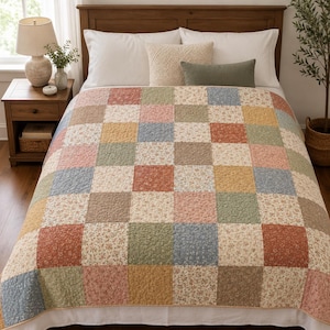 Puede incluir: Un edredón de patchwork en un dormitorio. El edredón presenta un patrón de cuadrícula de cuadrados en varios colores, incluyendo azul, rosa, amarillo y estampados florales. La cama tiene almohadas blancas y un cabecero de madera.