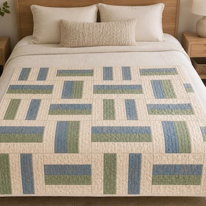 May include: A rectangular quilt featuring a geometric block pattern composed of cream, sage green, and dusty blue fabric segments. The quilt displays a repeating grid design with visible quilted stitching throughout the entire surface area.