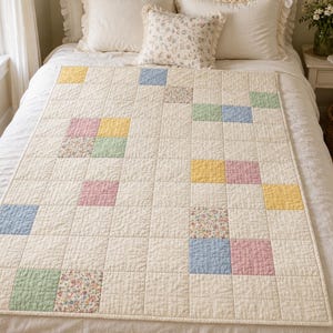 May include: A rectangular quilt featuring a grid of cream-colored fabric squares interspersed with scattered blocks in pastel yellow, light blue, soft green, dusty pink, and a multi-colored floral print, all finished with a simple cream-colored border.