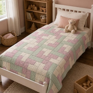 May include: A single-sized quilt featuring a geometric pattern of interlocking rectangles in soft shades of sage green, dusty rose, and cream. The quilt is draped over a white bed frame, with a light beige pillow and a small teddy bear resting on top.
