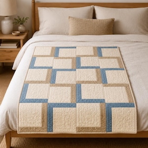 May include: A rectangular quilt featuring a geometric pattern of interlocking L-shaped blocks in shades of cream, tan, and dusty blue. The fabric has a visible quilted texture with stitched lines throughout the surface of the entire blanket.