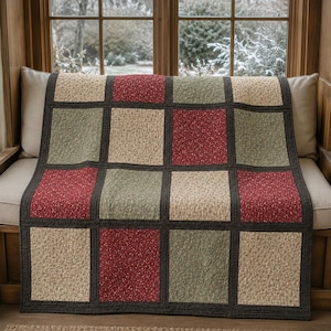 May include: A patchwork quilt featuring a grid of square fabric panels in alternating colors of deep red, sage green, and cream, each decorated with a small floral pattern. The squares are separated by dark charcoal gray fabric borders.