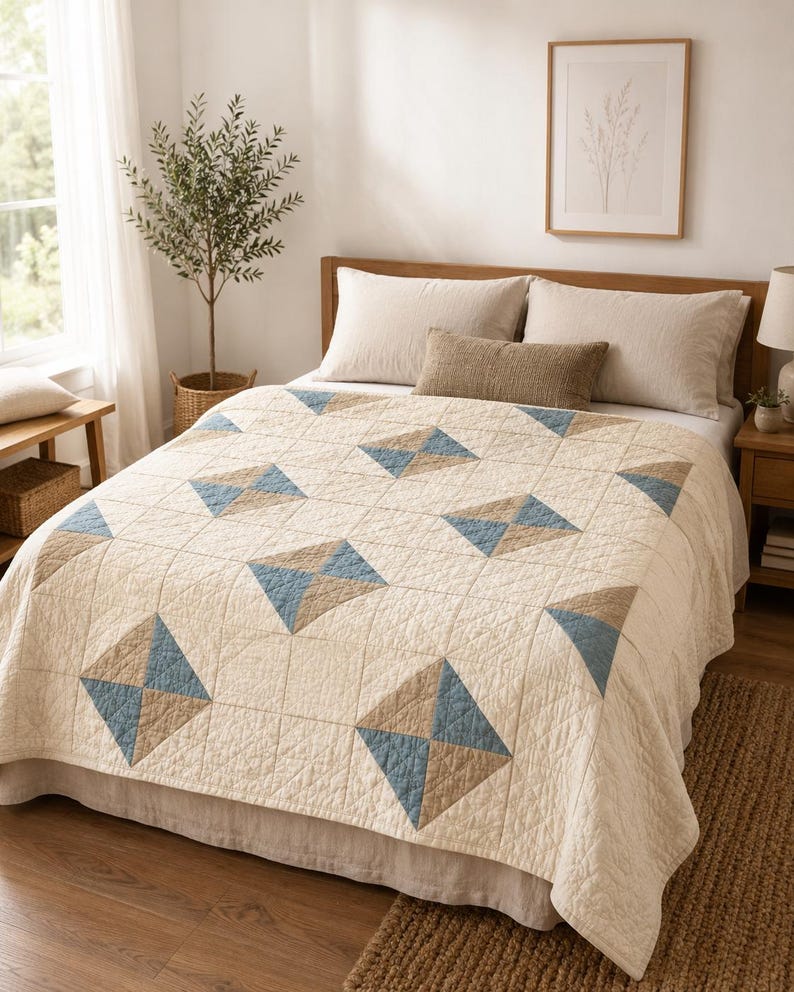 May include: A cream-coloured quilt featuring a repeating geometric pattern of squares divided into four triangles. Each square block alternates between solid cream fabric and a combination of two blue and two tan triangles, all with visible stitching.