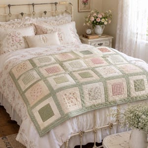 May include: A patchwork quilt featuring a grid of square blocks in shades of sage green, soft pink, and cream. The quilt displays a variety of patterns including floral prints, small gingham checks, and solid textures, all framed by green borders.