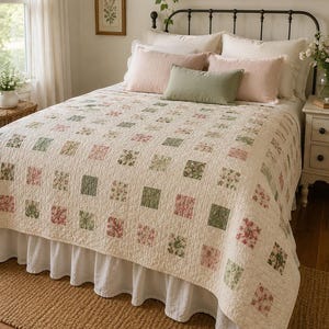 Puede incluir: Una colcha de color crema con una cuadrícula de pequeños parches cuadrados en tonos suaves de rosa y verde salvia con estampados florales. La colcha tiene una textura acolchada en forma de diamante y cubre una cama con volante blanco.