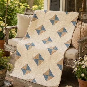 May include: A rectangular quilt featuring a cream-coloured background with a repeating geometric pattern of diamond shapes. Each diamond is divided into two triangles, one in muted blue and one in tan, with visible grid-like stitching throughout.