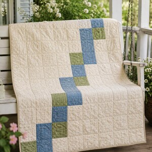 May include: A rectangular quilt featuring a cream-coloured background with a diagonal, stepped pattern of alternating blue and sage green square fabric patches. The quilt has a visible grid-like stitched texture throughout the entire surface.