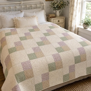 May include: A quilt featuring a repeating geometric pattern of cream, sage green, lavender, and tan squares. The cream squares have a subtle, embossed floral texture, while the colored squares display a delicate, small-scale floral print.