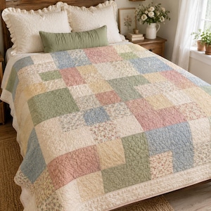 Puede incluir: Una colcha de patchwork con un patrón repetitivo de bloques cuadrados en tonos suaves de verde salvia, rosa empolvado, azul pálido y crema. La colcha muestra una mezcla de cuadrados de tela de color sólido y cuadrados con un delicado estampado floral.
