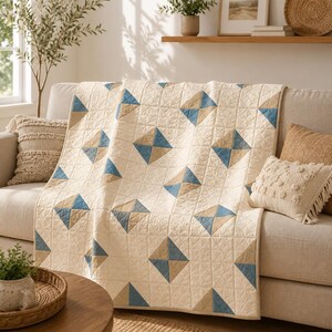 May include: A cream-coloured quilt featuring a repeating geometric pattern of blue and tan squares. The fabric has a visible quilted texture with intricate stitching throughout, creating a soft, layered appearance across the entire surface of the textile.