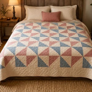 Puede incluir: Una colcha de cama con un patrón geométrico de triángulos alternos en tonos azul apagado, rosa viejo y crema. La tela tiene una textura acolchada visible en toda la superficie, cubriendo la cama con un diseño de bloques repetitivos.