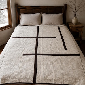 Peut inclure: Un couvre-lit couleur crème orné d'un motif à lignes droites marron foncé. Le couvre-lit est étalé sur un lit avec deux oreillers assortis de couleur crème. Le tissu présente une texture matelassée visible avec des lignes cousues.