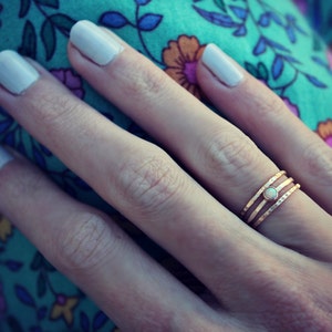 Può includere: Un anello d'oro con tre bande e una piccola pietra di opale bianca al centro.