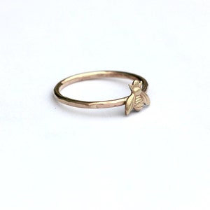 May include: A gold ring with a textured band and a small bee charm.