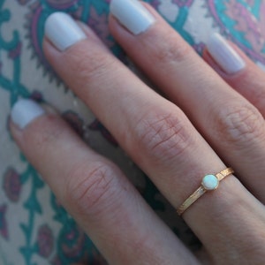 Puede incluir: Un anillo de oro con una piedra de ópalo blanco. El anillo está en el dedo de una persona.