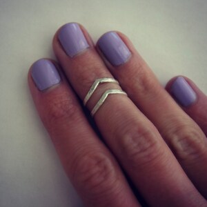 May include: A silver double chevron ring on a finger with lavender nail polish.