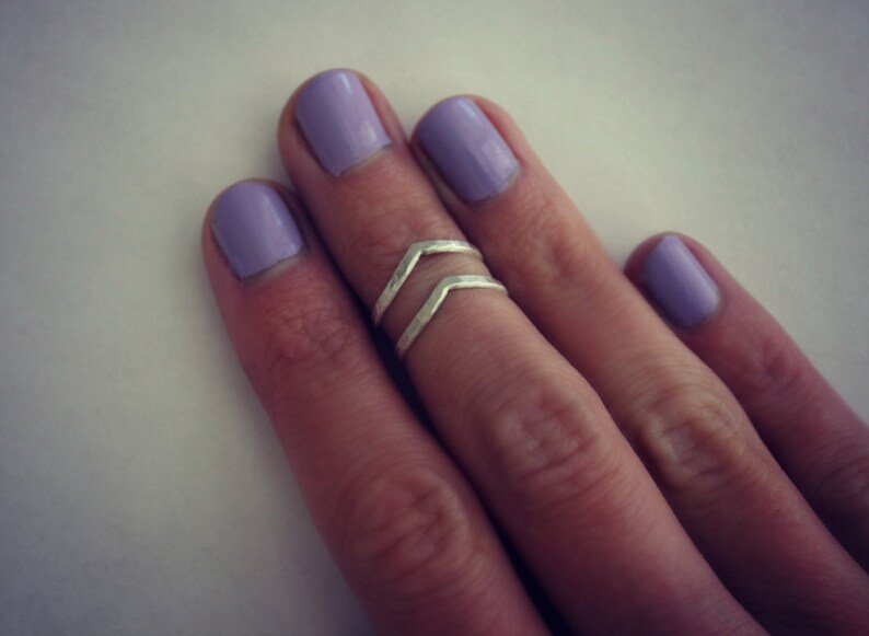 May include: A silver double chevron ring on a finger with lavender nail polish.