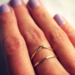 Könnte beinhalten: Ein goldener Ring mit einem Chevron-Design. Der Ring wird am Mittelfinger einer Hand mit helllila Nagellack getragen.