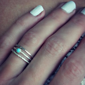 Puede incluir: Primer plano de una mano con tres anillos de plata. El anillo del medio tiene una piedra turquesa.