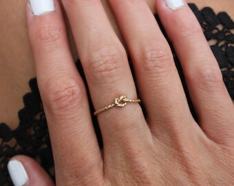 May include: A delicate gold ring with a knotted design. The ring is thin and simple, making it a subtle and elegant piece of jewellery.