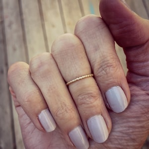 May include: A close-up of a hand wearing a thin gold band ring on the ring finger. The fingernails are painted a light nude color.