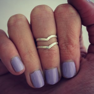 May include: A silver ring with a wavy design, worn on a finger with lavender nail polish.
