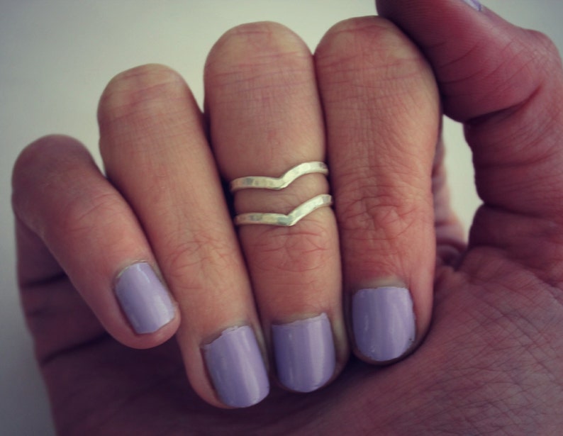 May include: A silver ring with a wavy design, worn on a finger with lavender nail polish.