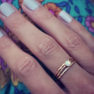 May include: A close-up of a hand wearing a gold ring with a white opal stone. The ring is a delicate, hammered band with a simple design.