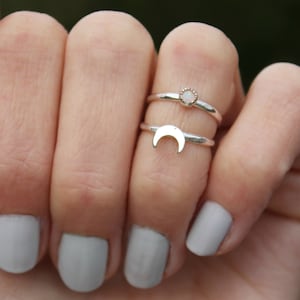 Könnte beinhalten: Zwei silberne Ringe an einem Finger. Der obere Ring hat einen kleinen weißen Opal-Stein. Der untere Ring hat ein Halbmond-Design.