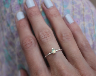 May include: A silver ring with a small, round, iridescent opal gemstone. The ring has a hammered texture.