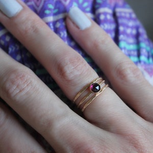 May include: A gold ring with three bands and a small, round, dark purple gemstone.