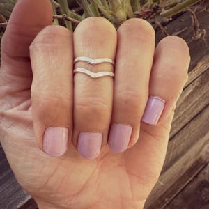 May include: A silver double chevron ring on a finger with light pink nail polish.