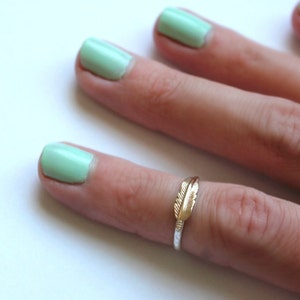 Könnte beinhalten: Ein goldener Federring an einem Finger mit hellgrünem Nagellack.