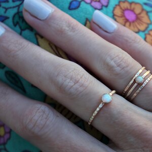 May include: Two gold rings with a white opal gemstone on a finger. The ring on the index finger is a simple band, while the ring on the middle finger is a triple band.