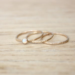 May include: Three gold rings with a hammered texture. The top ring has a small white opal gemstone.