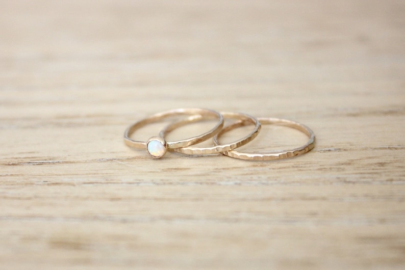 May include: Three gold rings with a hammered texture. The top ring has a small white opal gemstone.