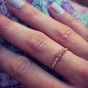 Può includere: Un anello d'oro con tre pietre rosa incastonate in un design a filo.