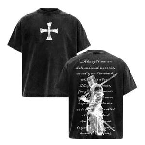 May include: A black acid-wash t-shirt featuring a white cross emblem on the front chest. The back displays a white graphic of a medieval knight holding a sword, overlaid with cursive text that reads: A knight was an elite medieval warrior.