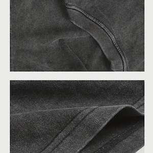 May include: A charcoal grey t-shirt featuring a washed, faded fabric texture. The garment displays a ribbed crew neckline and double-stitched hem detailing on the sleeves and bottom edge, showcasing the soft, worn-in appearance of the cotton material.