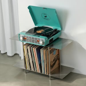 May include: A turquoise record player on a silver metal stand. The record player has a lid with a logo and a record on the turntable. The stand has two shelves filled with vinyl records.