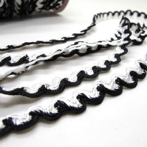 May include: Close-up of black and white wavy trim. The trim is made of a woven material with a scalloped edge. The trim is in a roll and several strands are unraveled, showing the detail of the design.