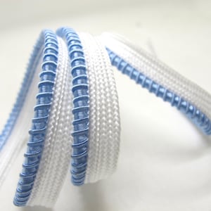 May include: Close-up of a white and blue decorative trim. The trim is white with a light blue, spiraled edge. The trim is coiled and curved, creating a textured and detailed appearance. Ideal for sewing and crafting projects.