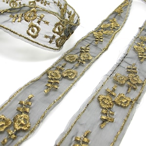 Pode incluir: Close-up de acabamento de renda preta com bordado floral dourado. A guarnição é feita de um tecido transparente e delicado e apresenta intrincados fios dourados. O design inclui padrões florais e de folhas.