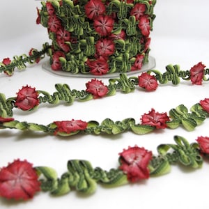 Op de afbeelding: Decoratieve band met rode bloemen en groene bladeren. De band wordt getoond in een rol en in strengen, waarbij het bloemmotief wordt benadrukt. Geschikt voor diverse knutselprojecten.