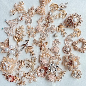 Puede incluir: Un surtido de adornos dorados y plateados, que incluyen diseños florales, de hojas y de mariposas. Muchas piezas presentan perlas y cristales transparentes. La colección incluye broches, apliques y elementos decorativos.