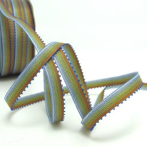 Peut inclure: Ruban rayé multicolore, bleu, jaune et orange. Le ruban a un bord texturé et est probablement utilisé pour l'artisanat, la couture ou l'emballage de cadeaux. La largeur du ruban est d'environ 1,5 cm.